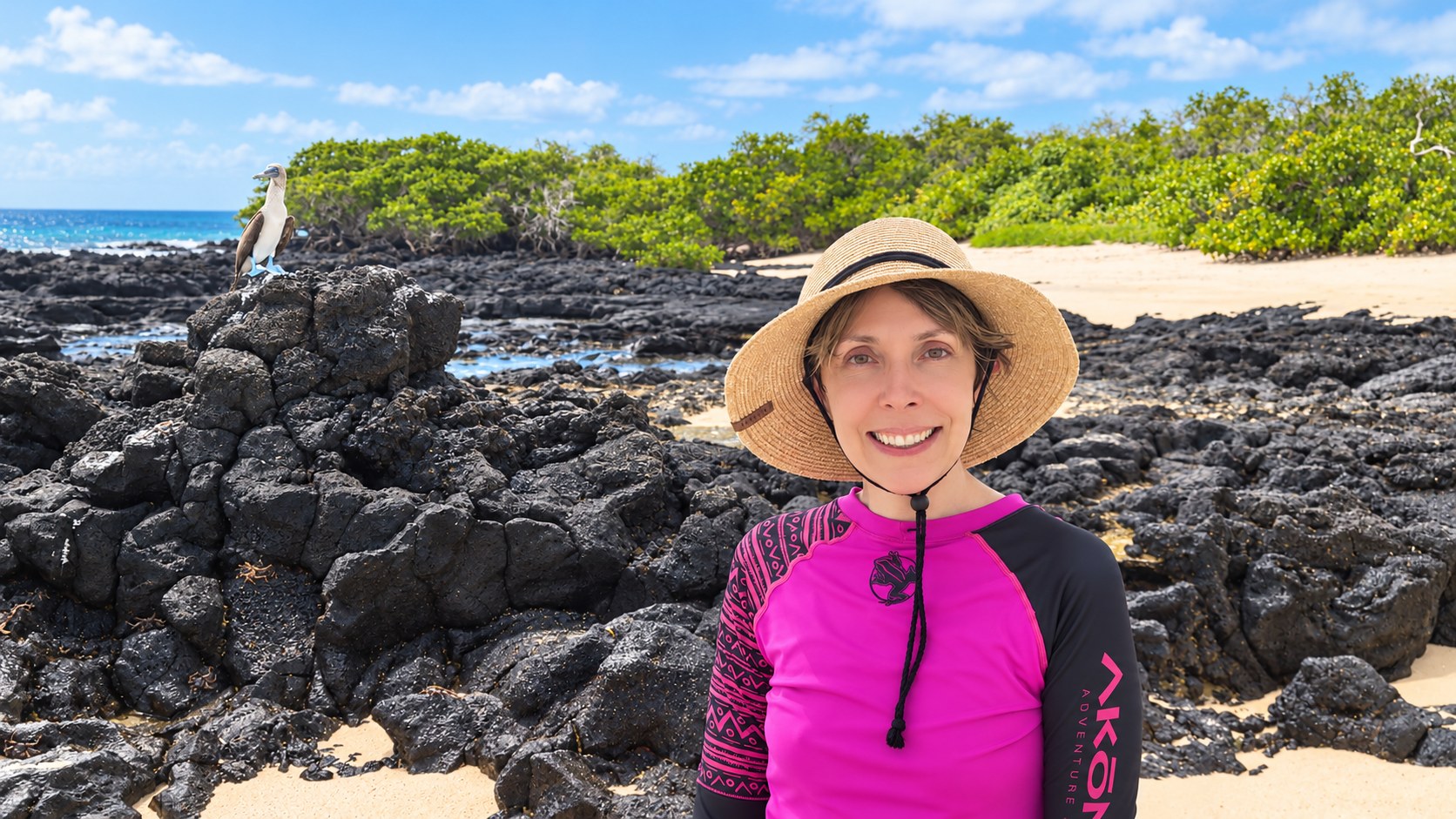 Michelle exploring the Galápagos Islands, with a blue-footed booby on the volcanic shore